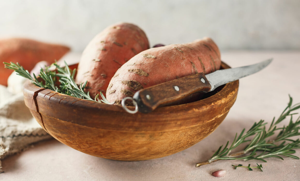 Wooden bowl filled with sweet potatoes, rosemary and a paring knife